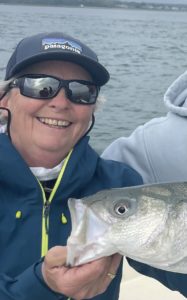 Capt. Avery holding a striped bass in front of a client holding a fly rod