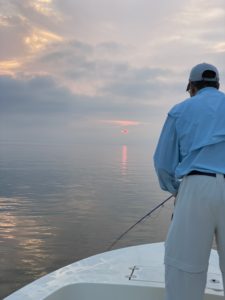 Late July Fishing Season, man fishing on a calm day with the sun rising in the background