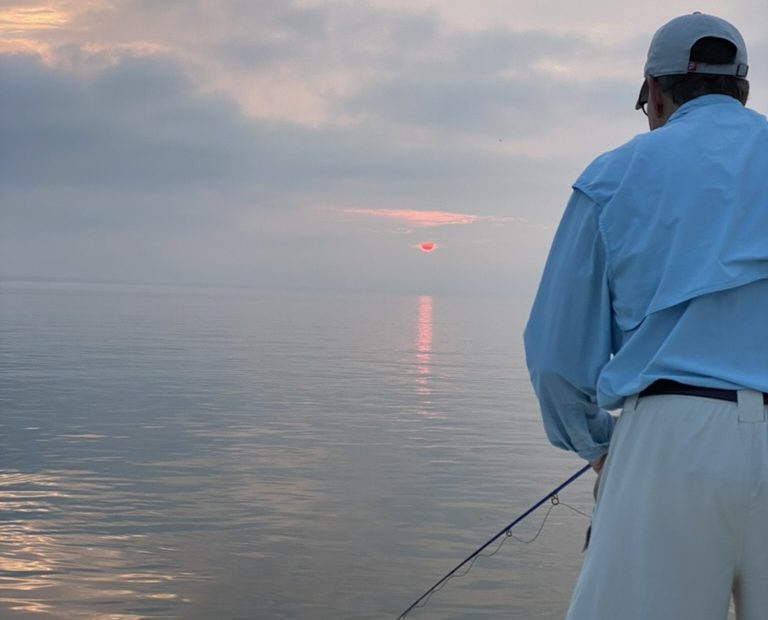 Late July Fishing Season, man fishing on a calm day with the sun rising in the background