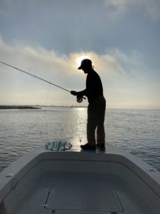 July Fishing Report: Silouetted man with fishing rod and halo of sun behind him