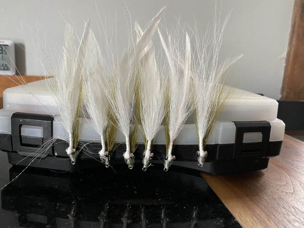 Fishing flies lined up.  Olive and white bucktail with white feathers.
