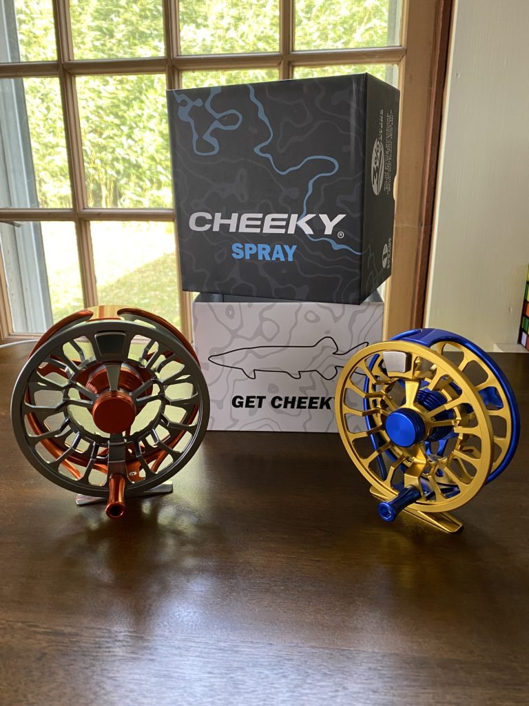 Two Cheeky Fly reels, one is oragne and silver, the other blue and gold